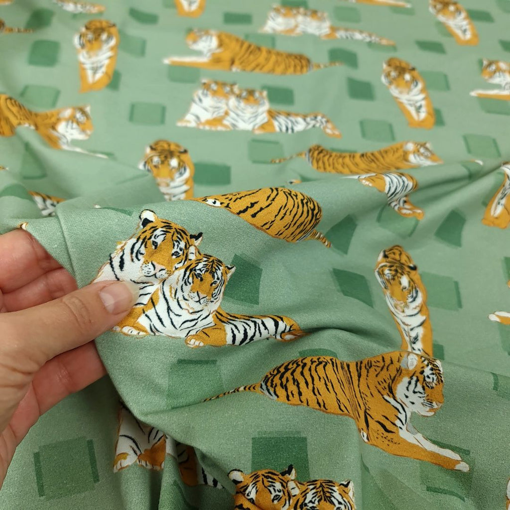 Det här single jersey trikå-tyget har ett mönster med tigrar på en mjuk grön bakgrund. Tyget er gjort av 95 % ekologisk bomull, 5 % elastan och känns mjukt och har en trevlig stretch vilket gör det perfekt för att sy bekväma barnkläder. Close-up.